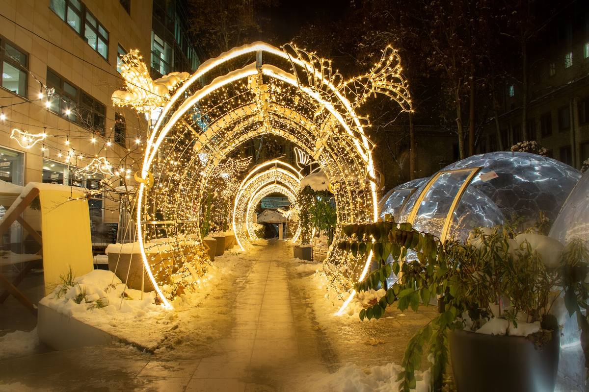 Svetlobni tunel z angeli in pticami v zasneženem mestnem okolju.